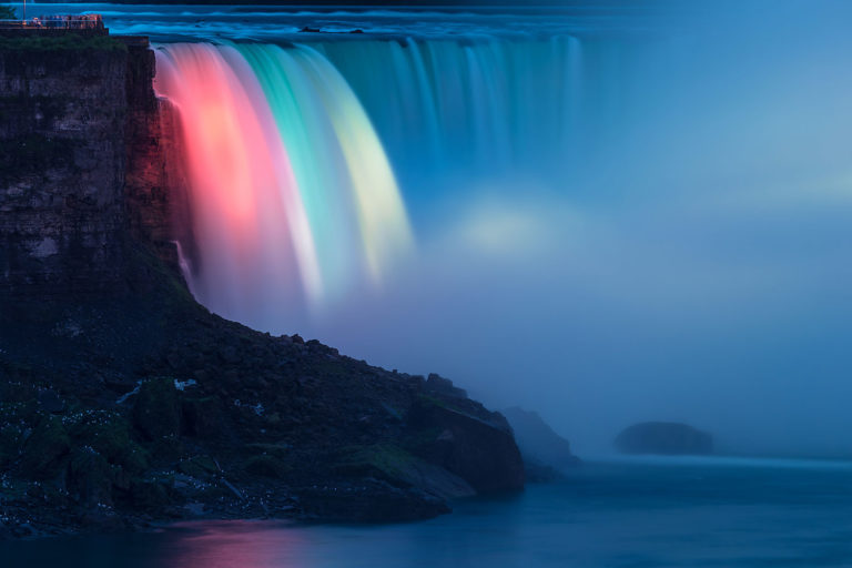 Niagara Falls - Illuminated Horseshoe Falls a.k.a. Canadian Falls as Seen from the Canadian Side in the Evening Every evening colorful lights illuminate the Falls. The rock on the left is Goat Island (United States). The white spots on the rock are birds.