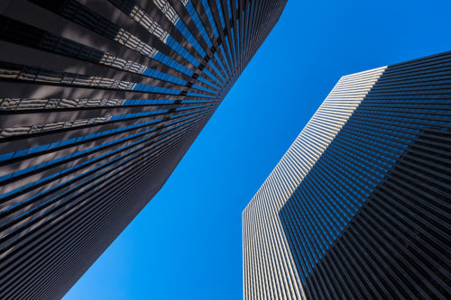 Upward view of two skyscrapers in New York City. One skyscraper casts a shadow onto the other one.